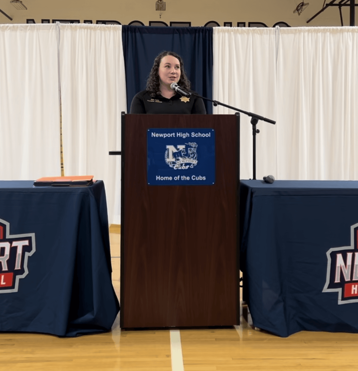 Woman in black shirt giving a speech behind a podium. 